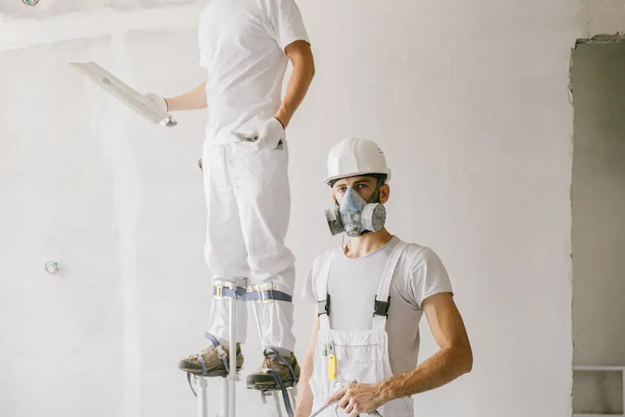 Two painters in white work clothes and respirators painting a large open interior