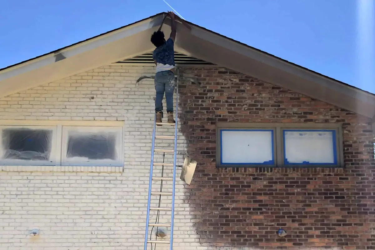 Our painter on a ladder spraying a brick home, with the windows and garage doors masked off